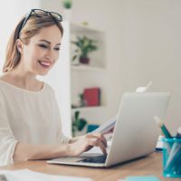 Uśmiechnięta kobieta korzysta z laptopa.