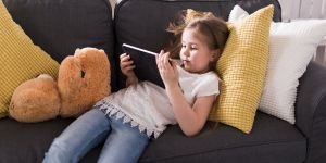 Dziewczynka leży na kanapie z tabletem w rękach.