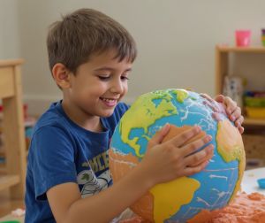 Uśmiechnięty chłopiec lepi z plasteliny kulę ziemską.