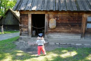 Małe dziecko stoi przed drewnianą chatą.
