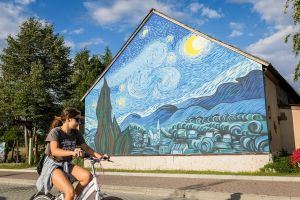 Na ścianie budynku mural z nocnym niebem i wioską w stylu Van Gogha.