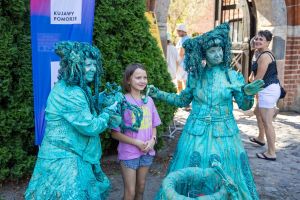 Dziewczynka pozuje do zdjęcia z dwiema kobietami przebranymi za pomniki.