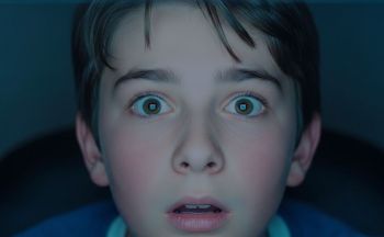 Twarz nastolatka z miną podekscytowania, zdziwienia, lęku. Ekran, na który patrzy odbija się w jego oczach.