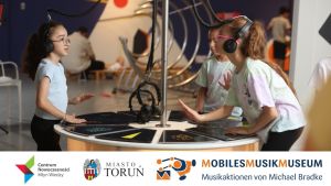 Trzy dziewczynki w słuchawkach na uszach stoją przy eksponacie