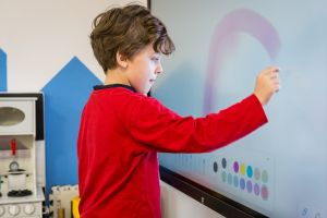 Czarnowłosy chłopiec stoi przed tablicą interaktywną.