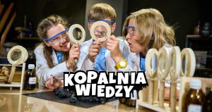 Troje uczniów w fartuchach laboratoryjnych przygląda się kawałkowi minerału przez lupy.