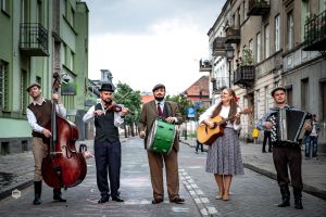 Czterech mężczyzn i jedna kobieta stoją na środku ulicy i grają na instrumentach muzycznych.
