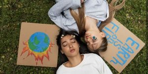 Dwie dziewczyny z zamkniętymi oczami leżą na trawie, przy głowach leżą rysunki, związane z ochroną ziemi.