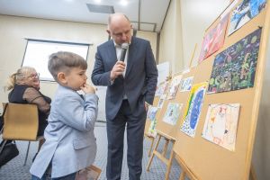 Marszałek województwa i chłopiec stoją przy tablicy, na której wiszą prace plastyczne.
