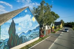 Ulica, drzewo oraz kilka domów, na jednym z domów jest mural inspirowany twórczością Van Gogha.