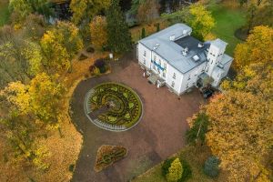 Widok z lotu ptaka na biały budynek wśród drzew w jesiennych kolorach.