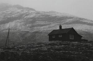 Czarno-białe zdjęcie, na których są góry i mały ciemny domek w ponurym klimacie.