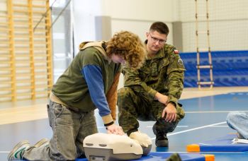 Żołnierz instruuje ucznia, jak na fantomie wykonywać masaż serca.