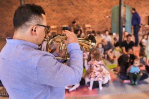 Mężczyzna gra na trąbce, w tle grupa dzieci.
