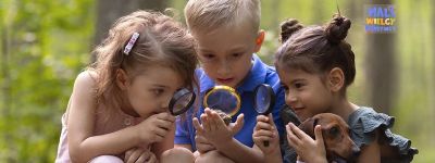 Troje przedszkolaków obserwuje z zaciekawieniem przez lupy minerał, który trzyma chłopiec.