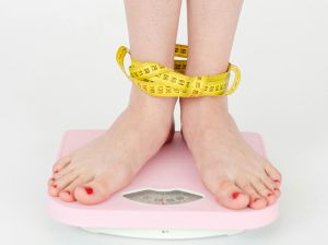 Waga domowa, na niej nogi dziewczyny, które są owinięte miarą krawiecką.