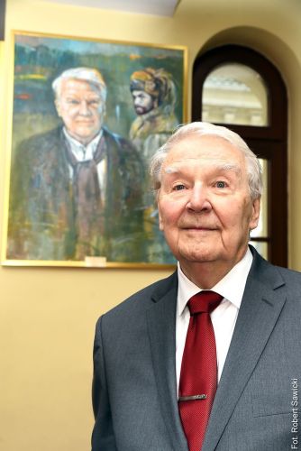 Mężczyzna stoi przed swoim portretem wiszącym na ścianie.