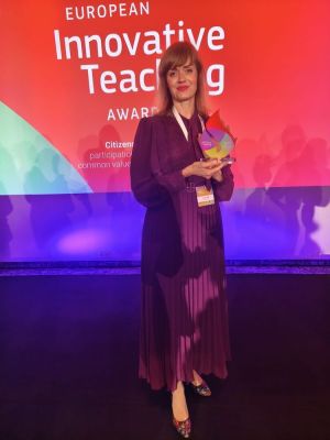 Kobieta trzyma statuetkę na tle banera European Innovative Teaching Award.
