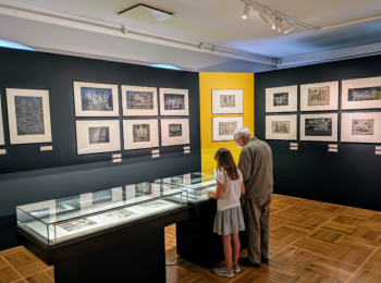 Starszy mężczyzna z dziewczynką oglądają grafiki w sali muzealnej.