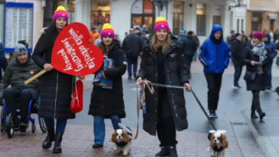 Trzy młode kobiety idą deptakiem z dwoma pieskami oraz dużym sercem WOŚP.