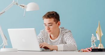 Nastolatek przy biurku z laptopem i lampą.
