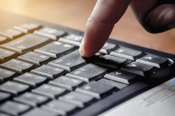 Klawiatura komputerowa i palec naciskający klawisz enter.