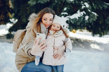 W zaśnieżonym lesie młoda kobieta robi zdjęcie sobie i małej dziewczynce.
