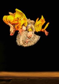 Osoba w barwnym stroju wykonuje akrobatyczne ćwiczenia.