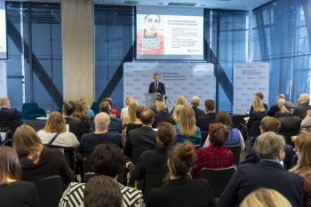 Prelegent przed ekranem z prezentacją i uczestnicy konferencji.
