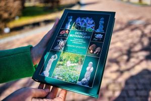 Książka pt. "Ogród botaniczny UKW..." w dłoniach człowieka w parku.