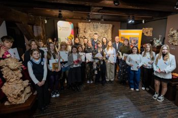 Grupa dzieci i młodzieży z opiekunami pozują do zdjęcia z nagrodami, w tle rzeźby.