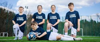 Dziewczęta i chłopcy w strojach piłkarskich pozują do zdjęcia na boisku.