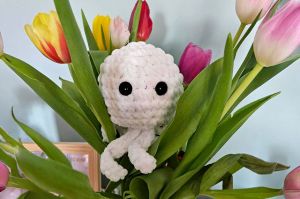 Stworek zrobiony na szydełku wśród kwiatów.