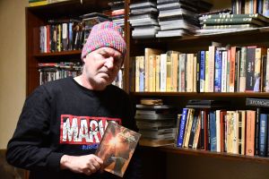 Mężczyzna w kolorowej czapce stoi przy regale z książkami.