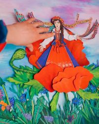 Zbliżenie na dłoń oraz wyciętą z papieru postać kobiety w stroju ludowym.