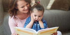Uśmiechnięta kobieta czyta dziewczynce książkę.