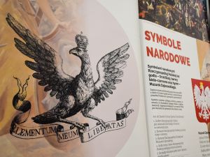 Orzeł w koronie ze wstęgą w szponach na planszy wystawy posterowej.