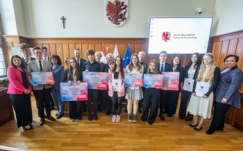 Młodzież i organizatorzy konkursu pozują do wspólnego zdjęcia pod herbem woj. kujawsko-pomorskiego.