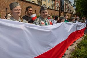 Harcerze i dorośli z flagami i chorągiewkami narodowymi.