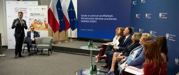 Urzędnicy ministerstwa siedzą w rzędzie. Za nimi ekran z prezentacją.