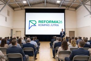 Prelegent z mikrofonem przed ekranem z logo Reforma26 Kompas Jutra oraz słuchacze siedzący na krzesłach.