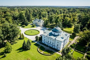 Biały pałac oraz mniejszy budynek wśród zespołu parkowego z lotu ptaka.