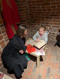 Kobieta i dziewczynka siedzą przy stoliku i przeglądają książkę.