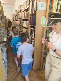 Dzieci przechodzą pomiędzy regałami bibliotecznymi.