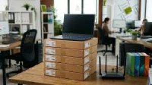 Stos laptopów na biurku, router i pudełka z oprogramowaniem.