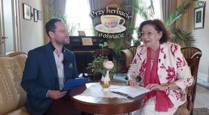 Prowadzący cykl "Przy herbacie o oświacie" siedzą przy stoliku w salonie z pianinem.