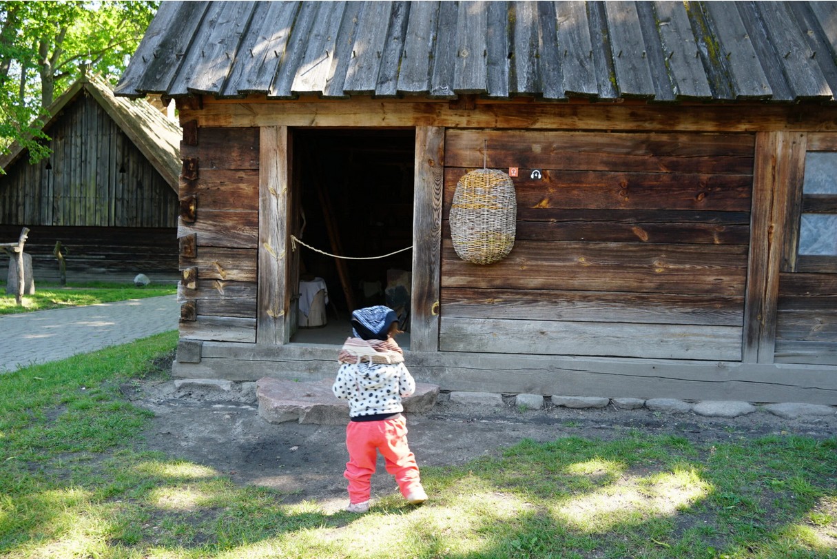 Małe dziecko stoi przed drewnianą chatą.