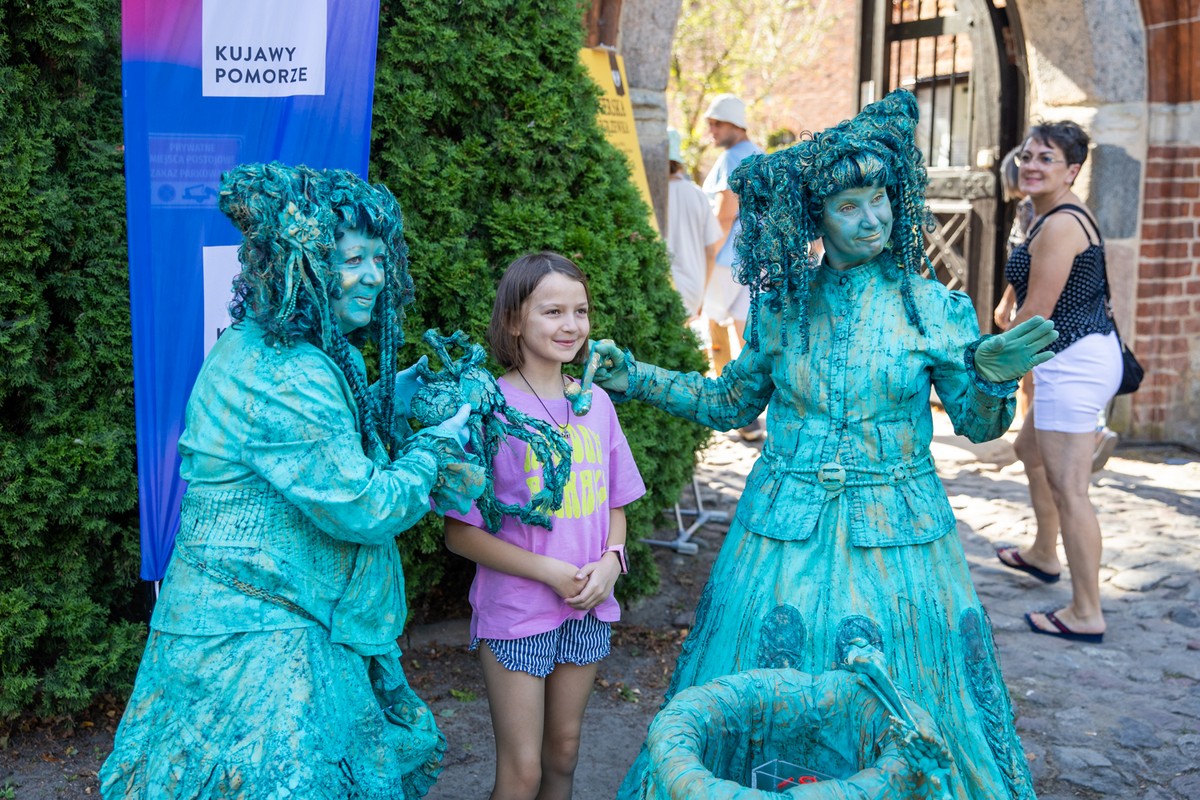 Dziewczynka pozuje do zdjęcia z dwiema kobietami przebranymi za pomniki.
