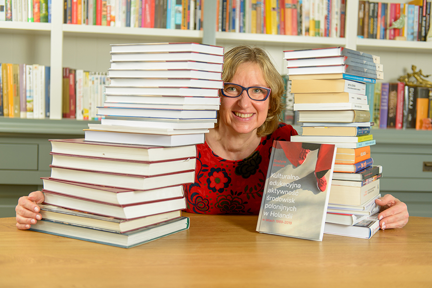 Uśmiechnięta kobieta siedzi przy stole z książkami.