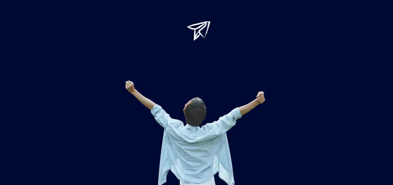 Widok z tyłu na chłopaka z uniesionymi rękoma. Nad jego głową leci samolocik z papieru.